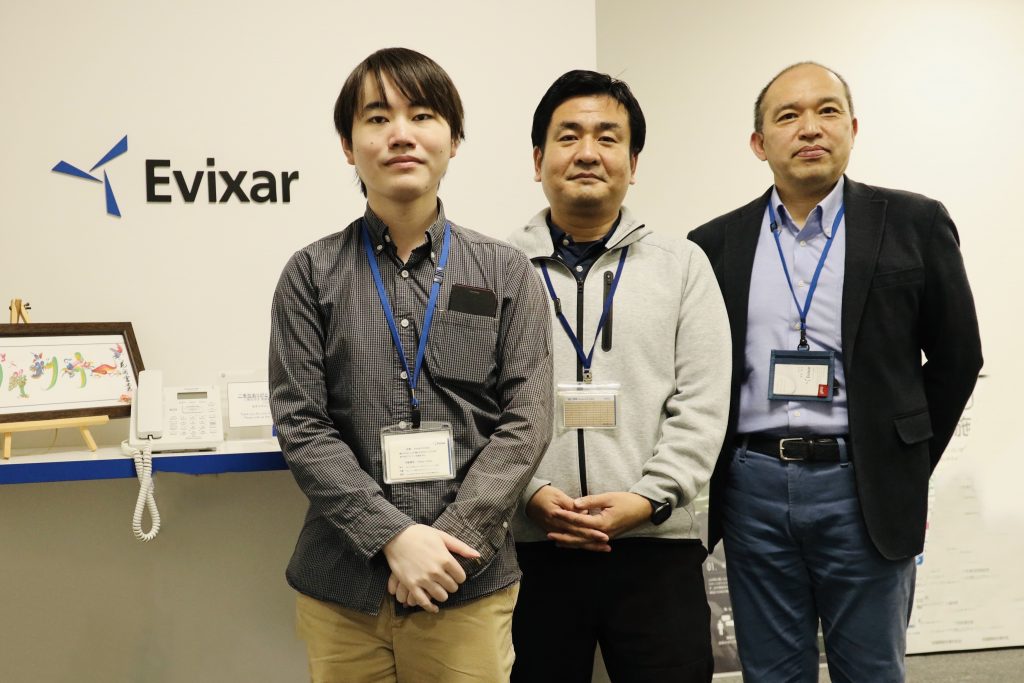 Photo of three people who work at Evixar standing in front of sign of Evixar.